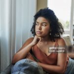 Shot of a young woman looking pensively out a window at home