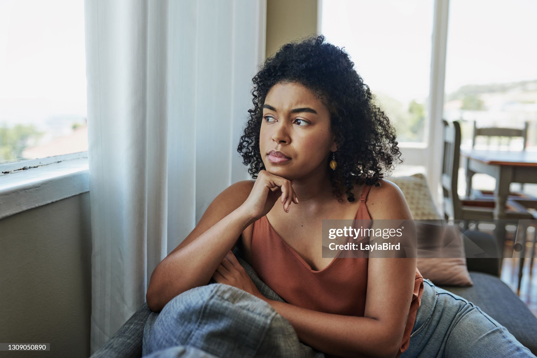 Shot of a young woman looking pensively out a window at home
