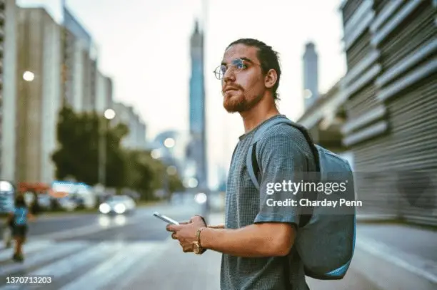 A young man standing alone in the city and looking contemplative
